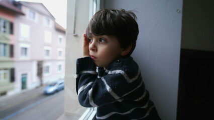 One bored child leaning on window looking out, little boy wanting to go outside. Sad depressed kid with nothing to do, staring at street from second floor home
