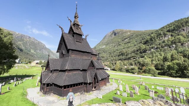 Young woman walking in summer towards the wooden church of Borgund, Norway