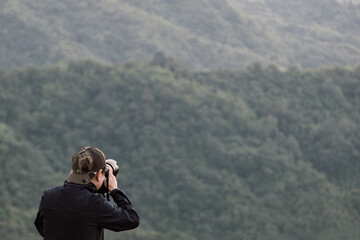 The photographer taking photo of mountain landscape with modern camera on tripod outdoors in the morning