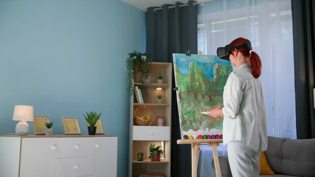 modern art, talented female artist draws picture with paints and spotting canvas while standing in viar glasses at home