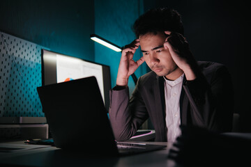 Stressed, tired business man suffering from headache, working late night in the office. Worried male entrepreneur thinking about problems and project deadline feeling burnout, stress and exhausted