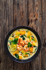 Thai soup with pumpkin, shrimps and coconut milk on wooden table
