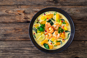 Thai soup with pumpkin, shrimps and coconut milk on wooden table
