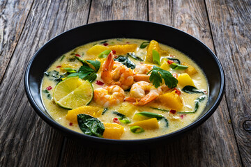Thai soup with pumpkin, shrimps and coconut milk on wooden table

