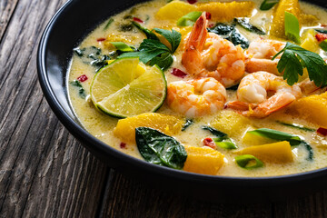 Thai soup with pumpkin, shrimps and coconut milk on wooden table

