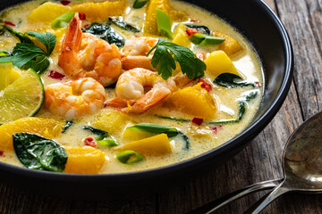 Thai soup with pumpkin, shrimps and coconut milk on wooden table
