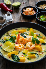 Thai soup with pumpkin, shrimps and coconut milk on wooden table
