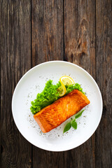 Seared salmon steak with lettuce and lemon on wooden table
