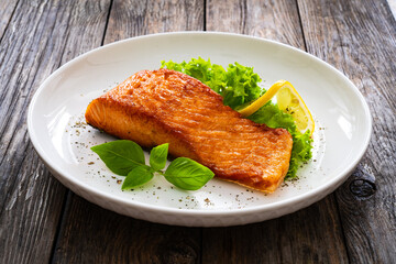 Seared salmon steak with lettuce and lemon on wooden table

