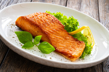 Seared salmon steak with lettuce and lemon on wooden table
