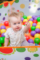 Fototapeta na wymiar The kid baby is having fun in a dry pool with balls. Having fun in playroom Leisure Activity.