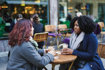 Young multiracial women drinking coffee together at bar outdoor during winter time
