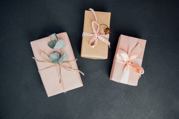 Background for greetings. Gifts wrapping in soft pink paper with dry eucalyptus branch on a black concrete background. Top view