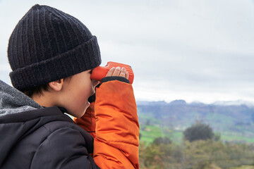 Surprised kid looking the meadow with binoculars during winter holidays