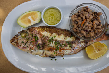 Delicious grilled whole sea bream with mustard sauce and citrus slices and small salad served on a plate in a greek tavern.
