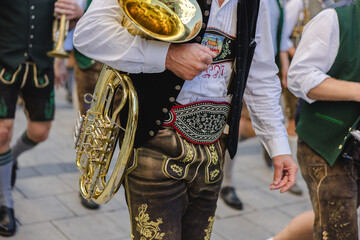 A man in traditional Bavarian attire carrying a wind instrument as part of a traditional brass band