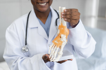 African American doctor woman holding bone foot model at hospital