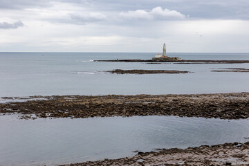 St. Mary's Lighthouse with basalt path at low tide with a series of basalt piers and a flat, calm sea just of the English coast. Whitley Bay, Newcastle, UK