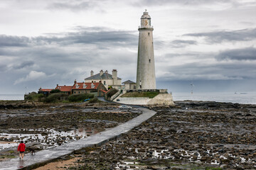 Fototapeta na wymiar St. Mary's Lighthouse with basalt path at low tide with a large offshore windmill at sea, for alternative green, renewable energy, electricity, just of the English coast. Whitley Bay, Newcastle, UK
