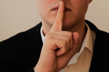A person in a suit places their index finger to their lips in close-up. Silence sign, a request for...