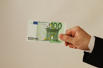 A person in a suit holds a one hundred euro banknote