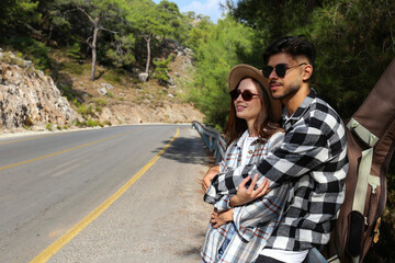 Happy couple of traveling musicians in checked flannel shirts hitchhiking on the empty switchback...