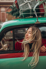 A blonde girl sits in a retro car decorated with Christmas gifts.