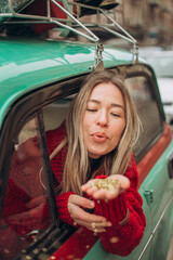 Young blonde woman peeking through a car window and blowing on a shining glitter confetti