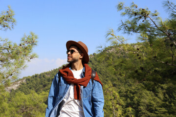 Bearded young man enjoying his hike in a mountain forest. Portrait of a hipster guy wearing casual outfit in the woods. Close up, copy space, background.