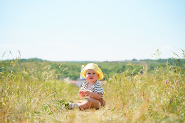 Naklejka na ściany i meble Cute baby child in panama is sitting in a field with dry grass and blue sky