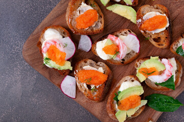 Assorted bruschetta with seafood, shrimp and caviar, avocado, cheese and radish on wooden board. Top view