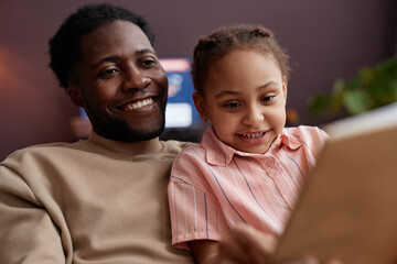 Close up portrait of Black father and daughter reading book together at home and enjoying family time