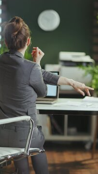 Sustainable Workplace. Seen From Behind Modern Small Business Owner Woman In A Grey Business Suit In Modern Green Office Stretching Hand.