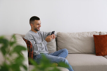 Bearded guy sitting on the corner couch with a phone. Relaxed man alone at home. Interior...