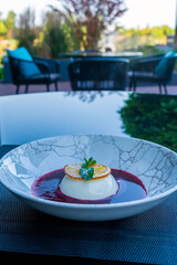 Italian dessert Panna Cotta in a plate on a table on the summer terrace of a restaurant.