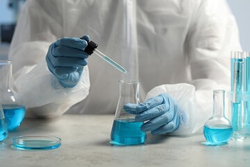 Scientist dripping liquid from pipette into beaker at white table in laboratory, closeup