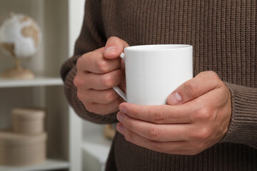 Man holding white mug indoors, closeup. Space for text