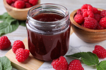 Delicious raspberry jam, fresh berries and green leaves on table