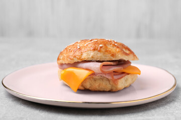 Delicious bagel with ham and cheese on light grey table
