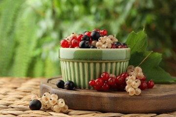 Different fresh ripe currants and green leaf on wicker surface outdoors, closeup