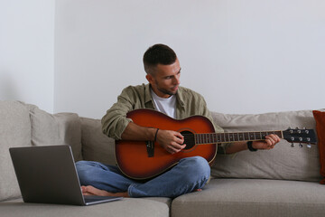 Bearded guy taking an online lesson on playing the acoustic guitar guitar on his laptop. Close up,...