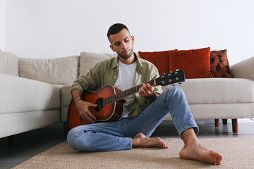 Young man sitting on the floor and playing dreadnought parlor acoustic guitar at home. Guitarist with sunburst colored instrument. Background, copy space, close up