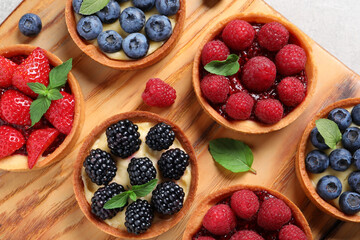 Tartlets with different fresh berries on wooden board, flat lay. Delicious dessert