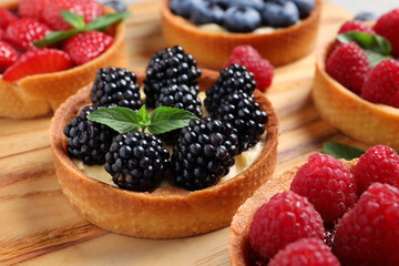Tartlets with different fresh berries on wooden board, closeup. Delicious dessert