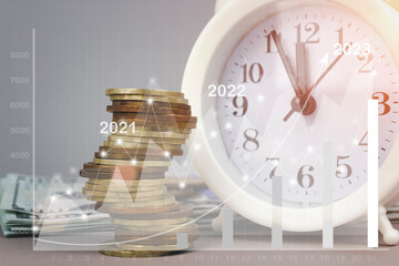 White alarmclock with Coins stack and stack of one hundred dollar bills with Financial charts...