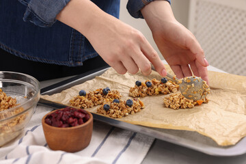 Obraz na płótnie Canvas Making granola bars. Woman putting mixture of oat flakes, dry fruits and other ingredients onto baking tray at table in kitchen, closeup