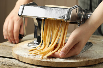 Woman making homemade noodles with pasta maker at wooden table, closeup - obrazy, fototapety, plakaty