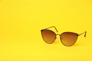 New stylish sunglasses on yellow background, space for text