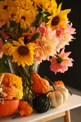 Autumn composition with beautiful flowers and pumpkins on white table near dark grey wall