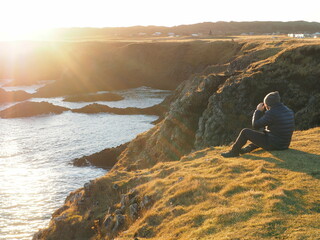 A person sitting on the coast facing the sun, watching the sea, representing:  future, career development, opportunities, financial planning, investment return, financial stability